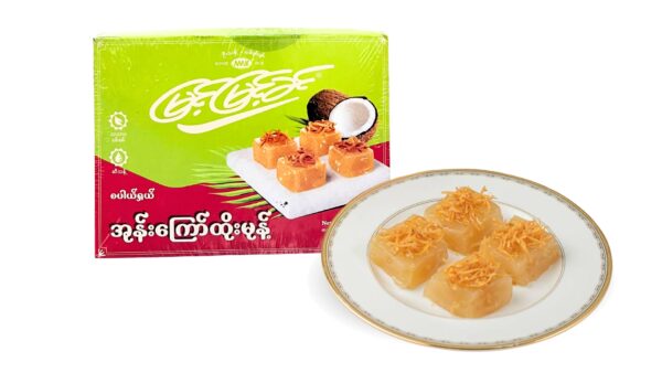 A green Myint Myint Khin box of fried-coconut Htoe Mont beside a gold-rimmed plate of translucent squares topped with toasted shredded coconut